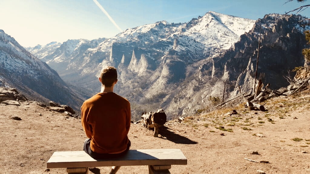 someone sits on a bench overlooking a snow-capped mountain view