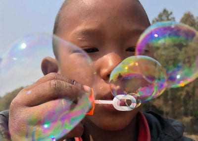 A little boy leans close to the camera blowing bubbles from a wand