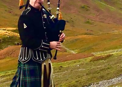 Bagpiper plays in front of a green grass hill