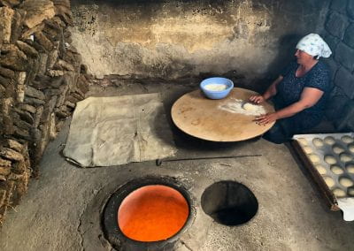 Woman wearing a bandana and sitting on a stone floor making traditional Armenian bread