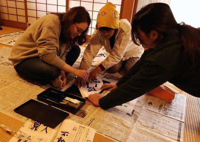 Three women gather, sitting on top of newspaper as they paint calligraphy characters