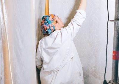 Woman in white smock delicately paints the wall with white paint.