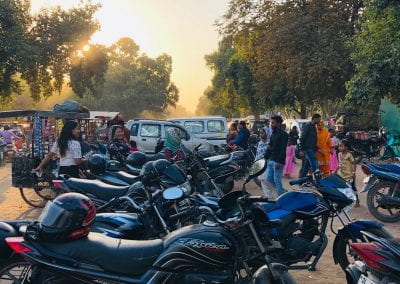A large collection of motorcycles stand outside in the setting sun.