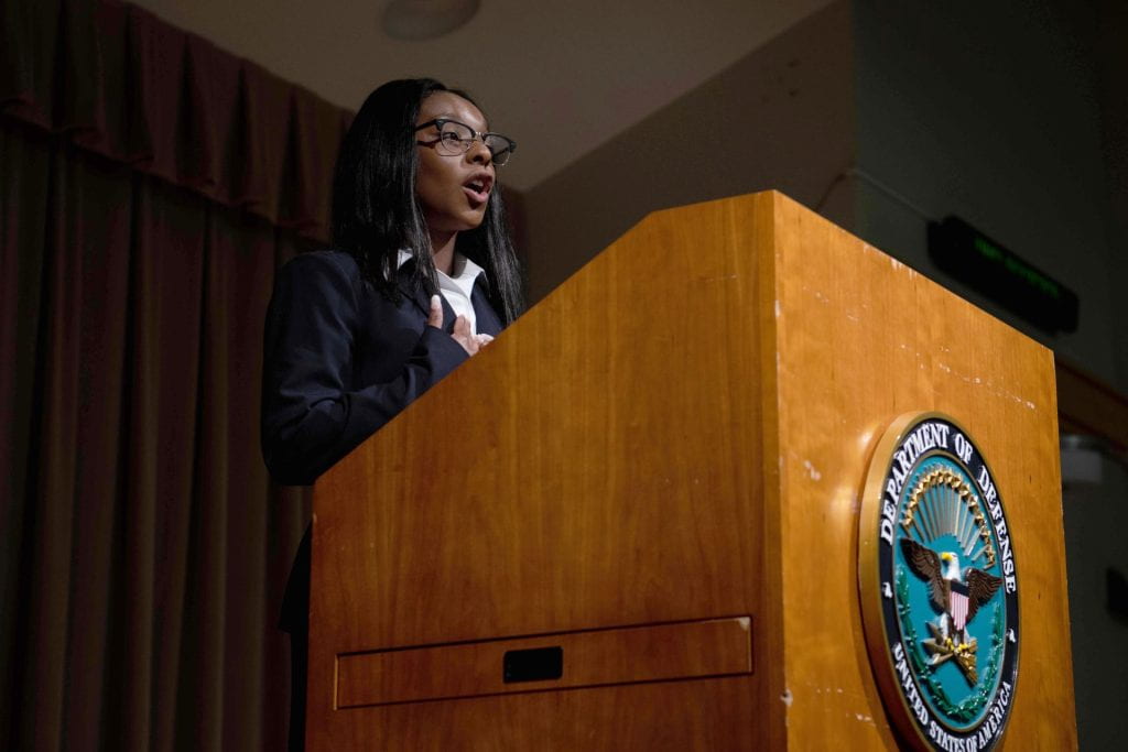 Dasia Bandy speaking at podium with the Department of Defense logo on the front of it.
