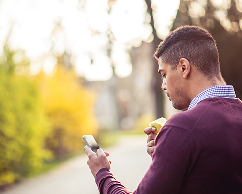 Man texting on his mobile phone and having a snack.