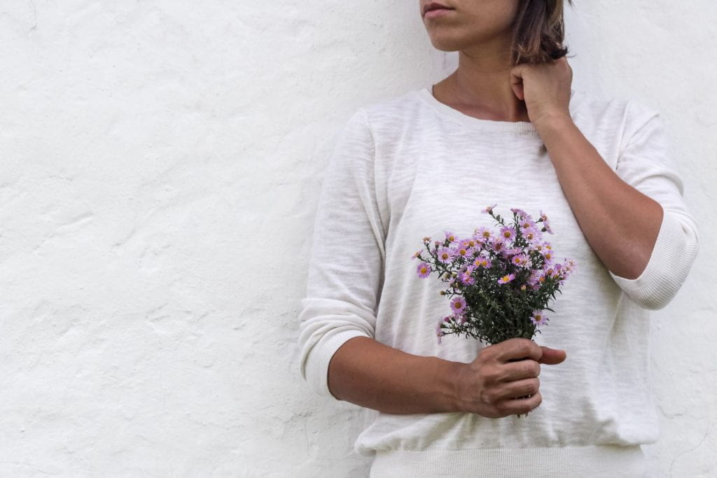 Woman standing in front of a wall holding flowers.