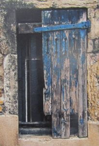 Photo of a weathered, blue shutter set in a stone wall.