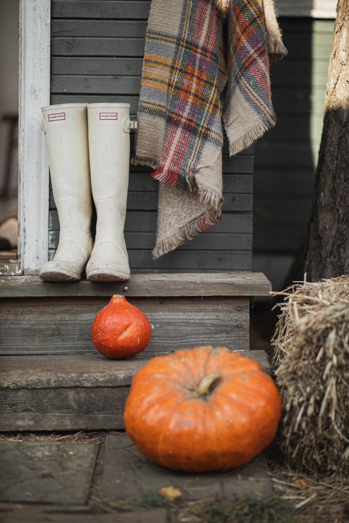 Photograph of the corner of steps leading to a door. On the ground is a medium sized pumpkin. On the first steps is a smaller pumpkin. White boots sit on the topmost step.