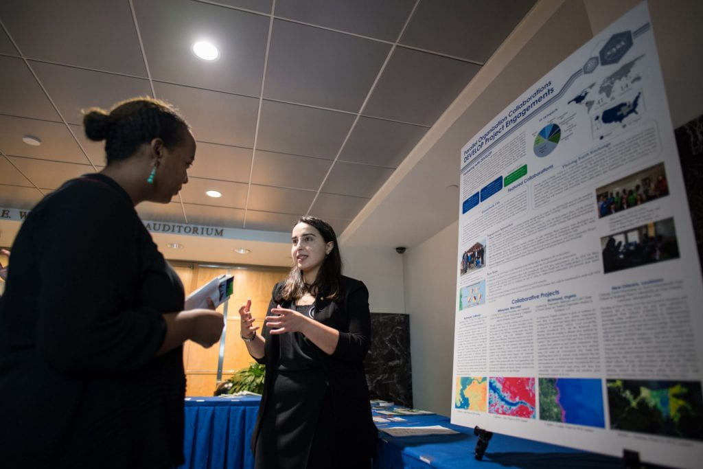 Photo of a woman presenting her research poster to another woman.