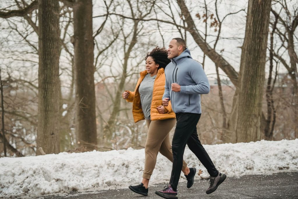 Black couple jogging on walkway during winter with snow in the background