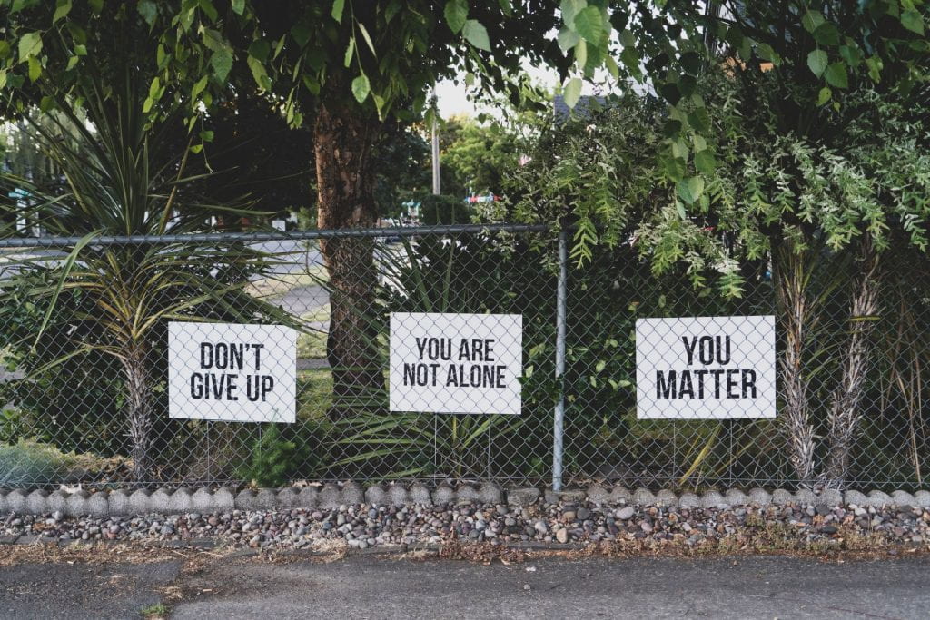 Image of signs posted behind a chain link fence. Signs read: "Don't give up" "You are not alone" "You matter"