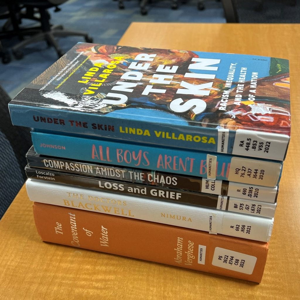 Photo of books stacked with spines showing titles displaying. 
