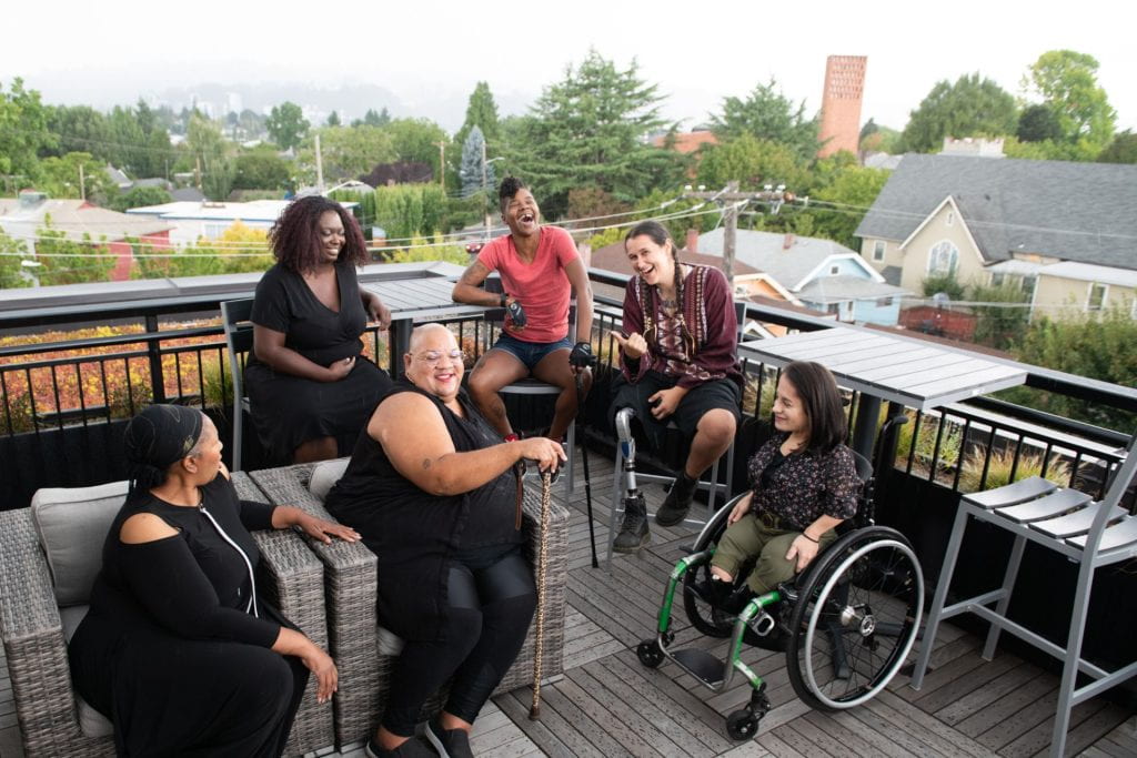Overhead shot of six disabled people of color at a rooftop deck party. 