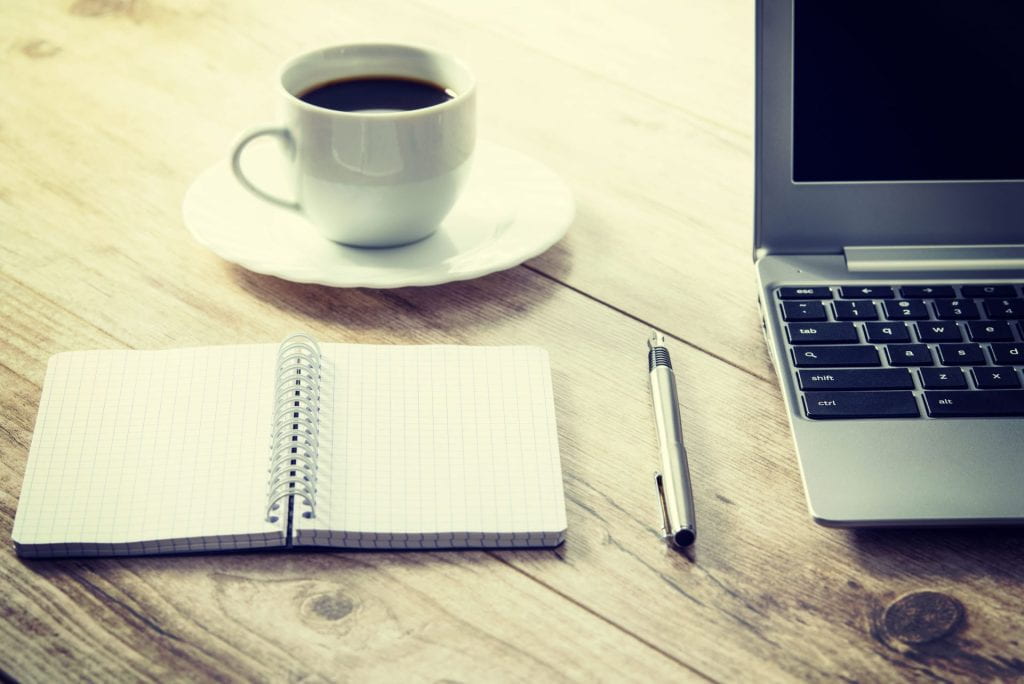 photo of coffee in teacup with open notebook, pen and laptop