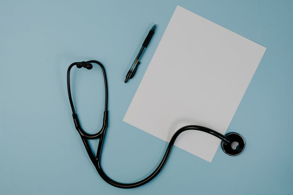 Decorative image of a black stethoscope, a blank sheet of white paper, and a black pen over a light blue background.