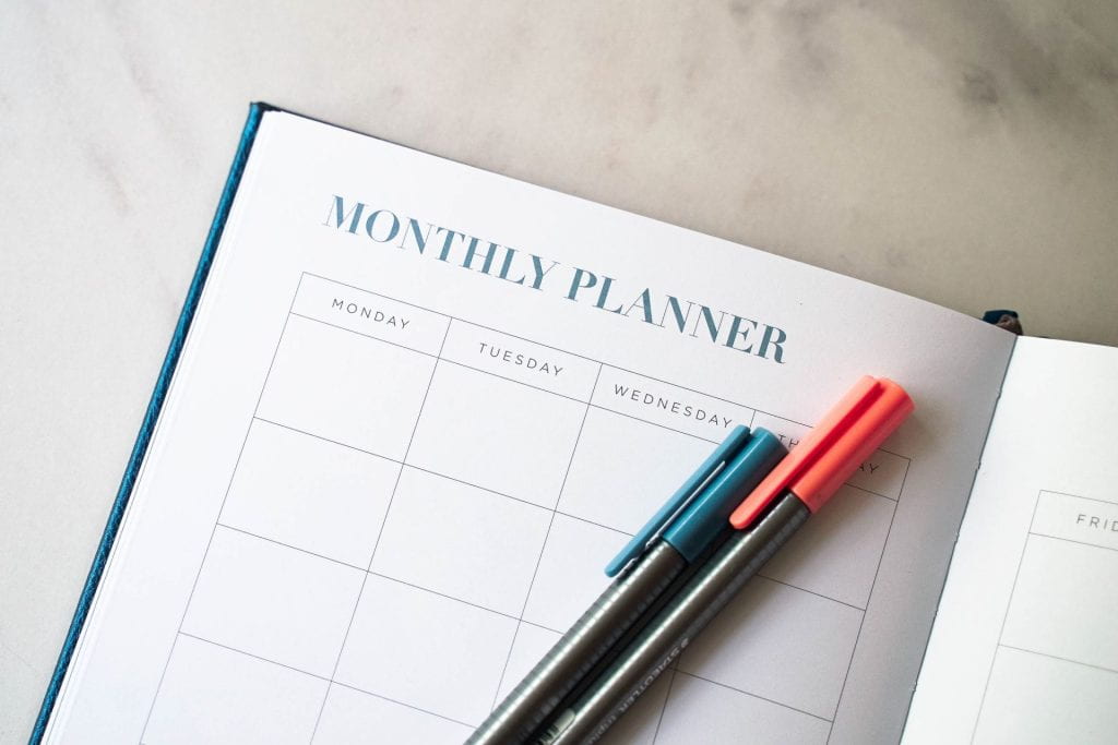 Picture of a monthly planner with a red and blue pen lying on top.