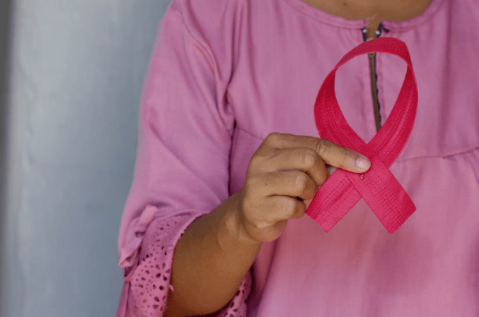 Picture of a brown woman wearing a pink shirt holding a pink ribbon.