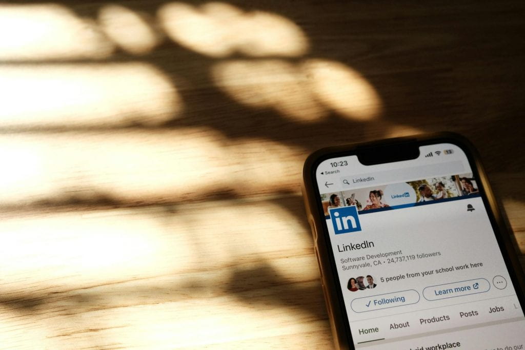 A phone screen that is open to a page on LinkedIn. In the background, sunlight shines on a wooden surface.