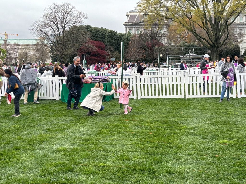 On the White House lawn, a child high fives an adult at the 2024 White House Easter Egg roll.