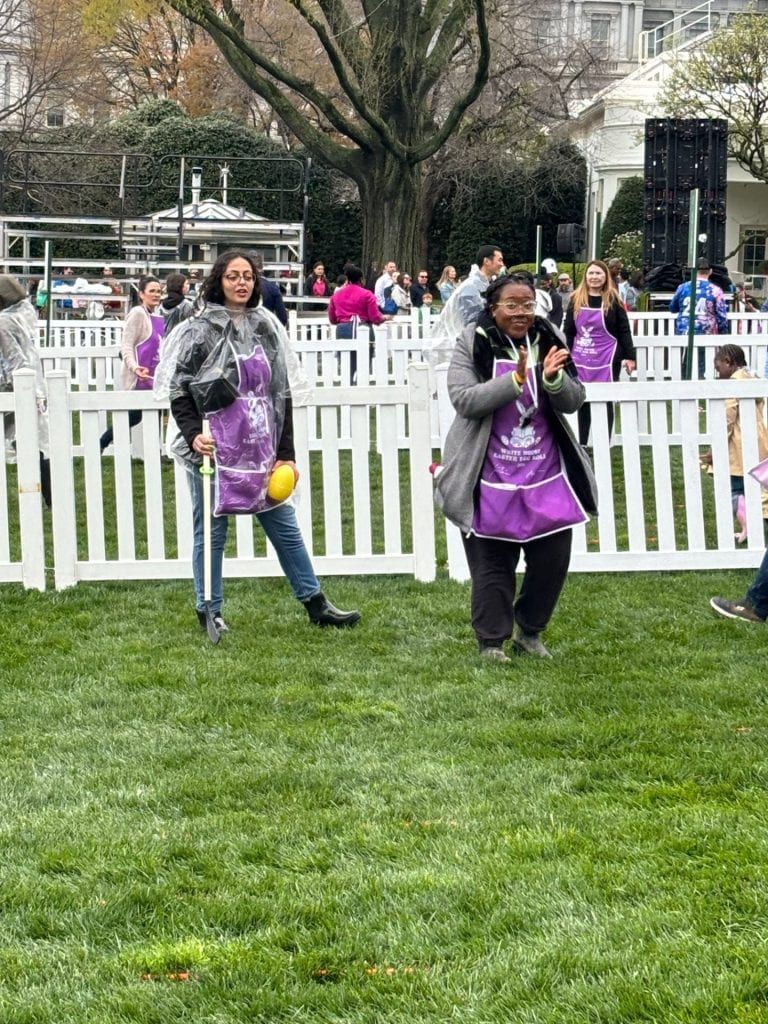 Two adults standing on a lawn looking during the 2024 White House Easter Egg Roll. One adult is applauding.