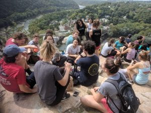 a group of students sit and laugh together as they take in the view from atop Harper's Ferry