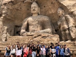 group photo in front of  massive stone buddha statues carved into a grotto